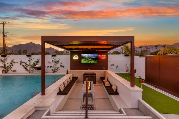 Resort swimming pool with turquoise water, lime-green lounge chairs, white walls, and desert mountains in background