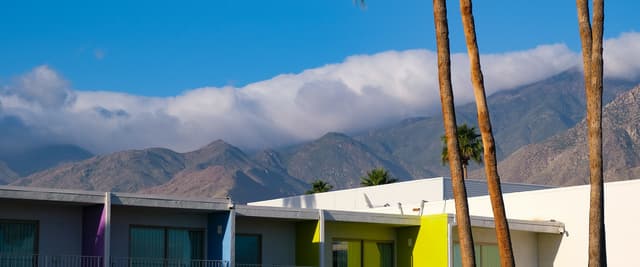 Palm Springs hotel courtyard with tall palms, bright blue sky, and the San Jacinto Mountains behind