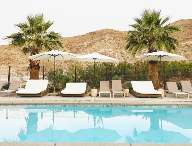 Palm Springs pool with lounge chairs, white umbrellas, and desert mountains in the background